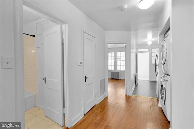 hallway featuring light wood-type flooring, stacked washer and dryer, and radiator