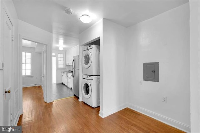 clothes washing area with stacked washer / drying machine, electric panel, and hardwood / wood-style flooring