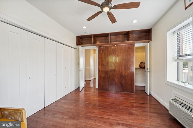 unfurnished bedroom featuring multiple windows, an AC wall unit, dark hardwood / wood-style floors, and ceiling fan