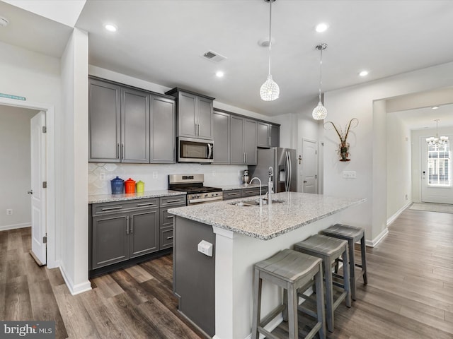 kitchen featuring light stone countertops, sink, stainless steel appliances, an island with sink, and pendant lighting