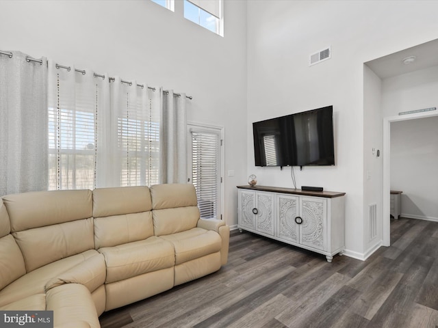 living room with dark hardwood / wood-style floors, a healthy amount of sunlight, and a towering ceiling