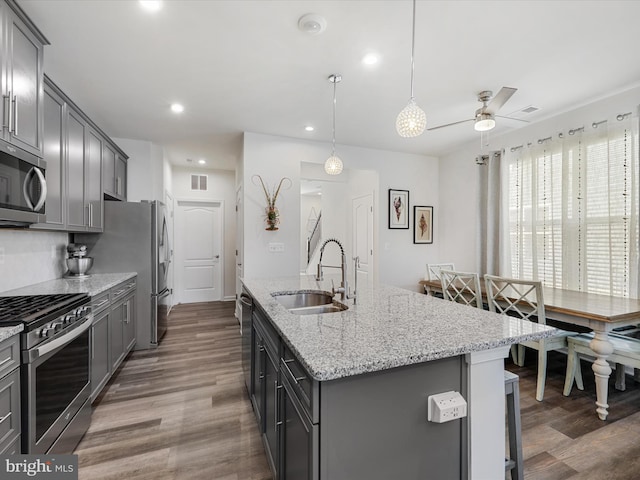 kitchen featuring dark hardwood / wood-style flooring, sink, appliances with stainless steel finishes, and an island with sink