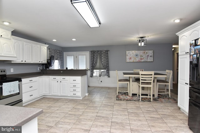 kitchen with white cabinetry, stainless steel electric range oven, kitchen peninsula, and black fridge