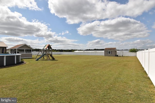 view of yard featuring a storage unit, a fenced in pool, and a playground