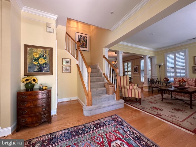 foyer entrance featuring ornamental molding, stairway, wood finished floors, and ornate columns