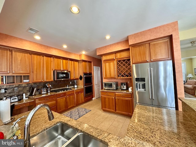 kitchen featuring stainless steel appliances, brown cabinets, a sink, and tasteful backsplash