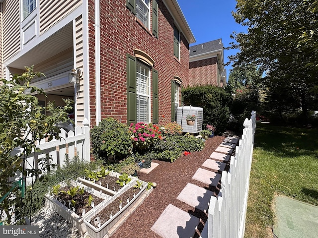 view of property exterior featuring brick siding, a vegetable garden, central AC, and fence