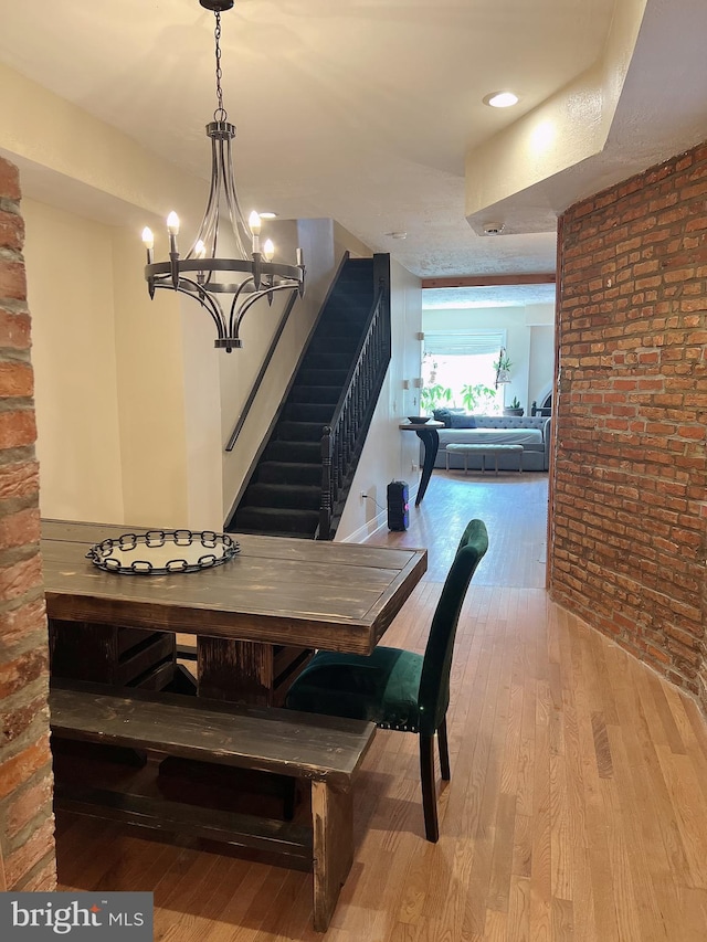 dining area featuring light wood-type flooring, a notable chandelier, and brick wall