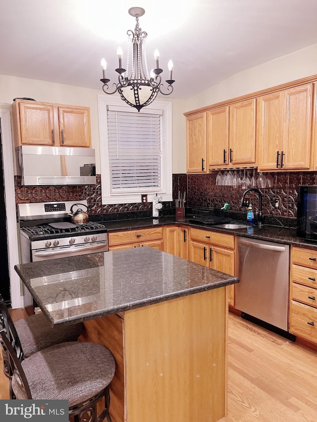 kitchen with stainless steel appliances, dark stone counters, a chandelier, a kitchen island, and light wood-type flooring