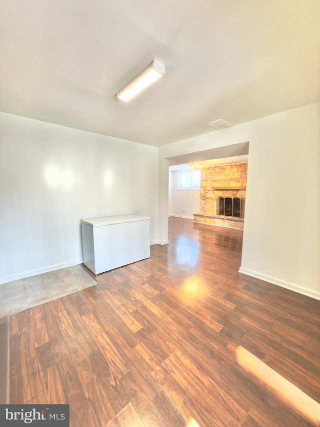 empty room featuring a stone fireplace and dark wood-type flooring