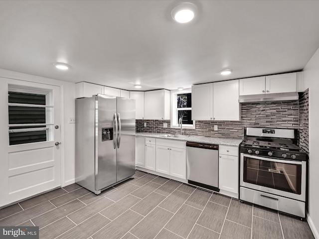 kitchen featuring sink, tasteful backsplash, white cabinetry, stainless steel appliances, and light stone countertops