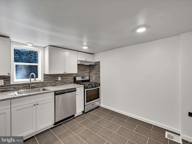 kitchen with sink, light stone countertops, backsplash, appliances with stainless steel finishes, and white cabinetry