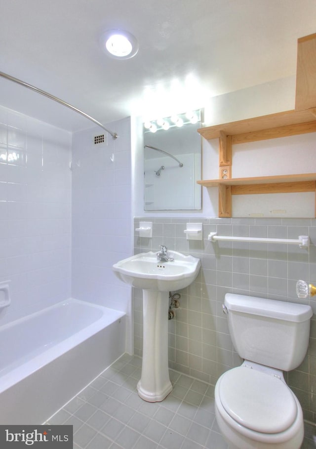 bathroom with toilet, tile patterned floors, tiled shower / bath, tasteful backsplash, and tile walls