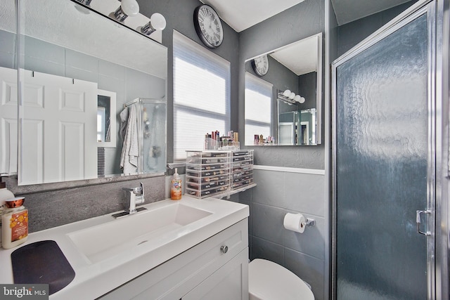 bathroom featuring vanity, toilet, tile walls, and a shower with shower door