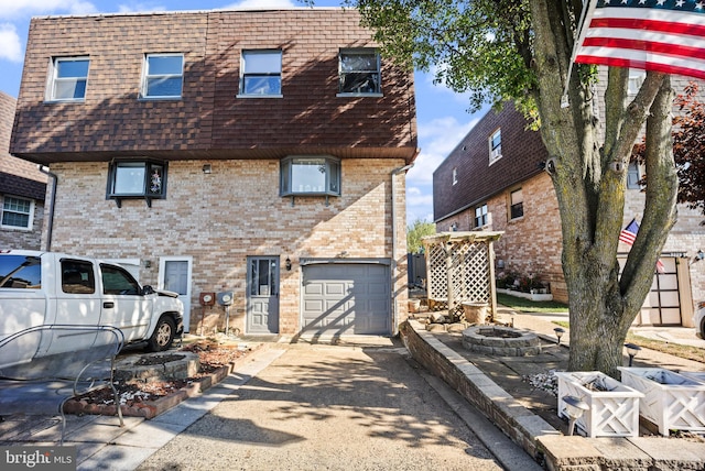 view of front facade featuring mansard roof, a fire pit, roof with shingles, concrete driveway, and brick siding