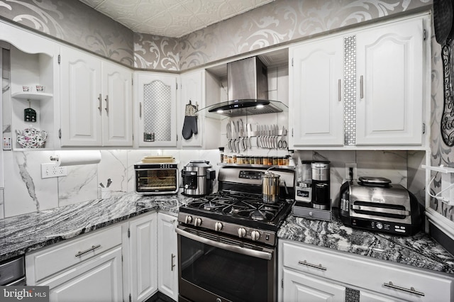 kitchen with tasteful backsplash, wall chimney range hood, dark stone counters, stainless steel gas range, and white cabinetry