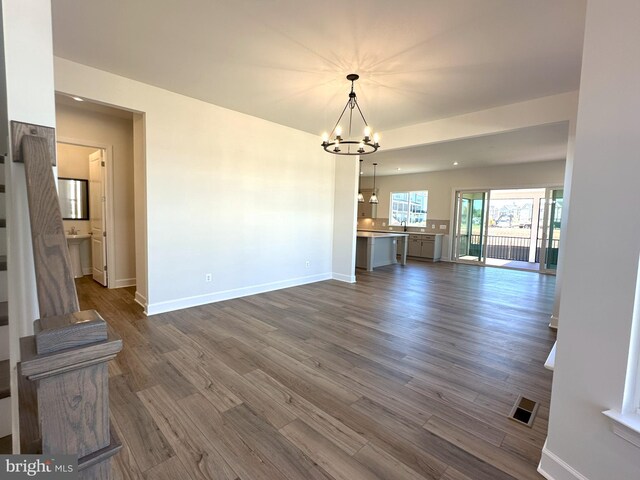 unfurnished living room featuring an inviting chandelier and dark hardwood / wood-style flooring