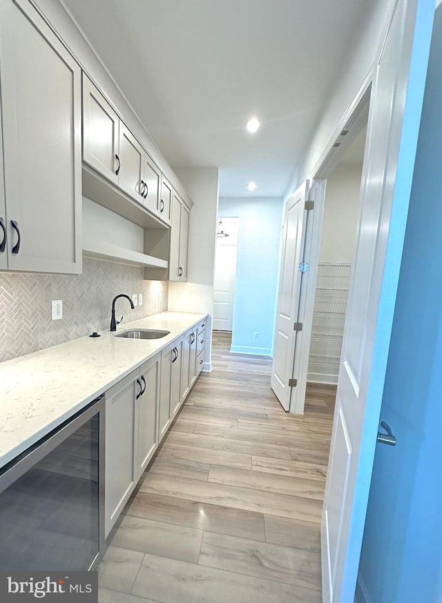 kitchen with tasteful backsplash, wine cooler, light stone counters, sink, and light hardwood / wood-style floors