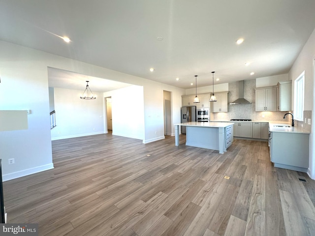 kitchen with a sink, decorative backsplash, light countertops, wall chimney exhaust hood, and stainless steel fridge