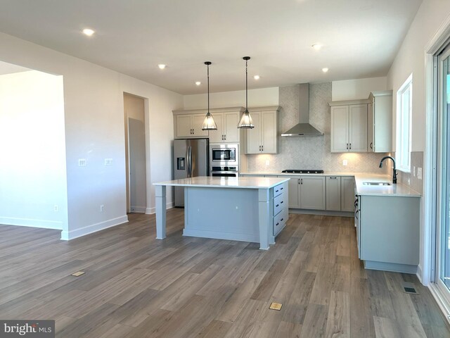 kitchen with wall chimney range hood, wood-type flooring, a kitchen island, and appliances with stainless steel finishes