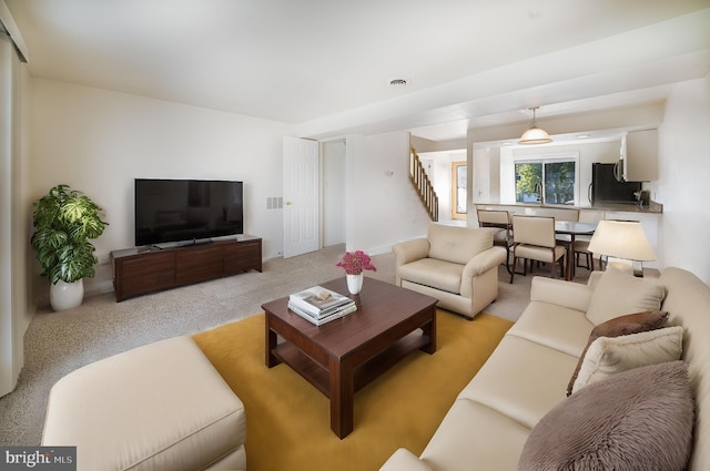 living room featuring stairway, light colored carpet, and visible vents