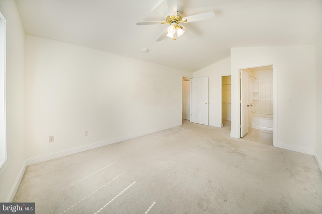 unfurnished bedroom with ceiling fan, ensuite bathroom, a spacious closet, light colored carpet, and vaulted ceiling