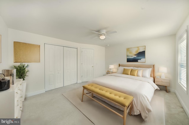 bedroom with ceiling fan, two closets, and light carpet