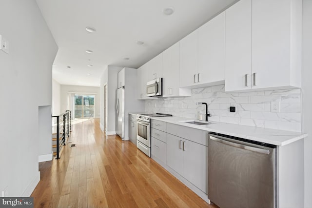 kitchen featuring stainless steel appliances, white cabinetry, sink, light wood-type flooring, and decorative backsplash