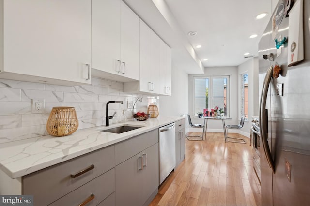 kitchen with light hardwood / wood-style floors, stainless steel appliances, light stone counters, white cabinets, and sink