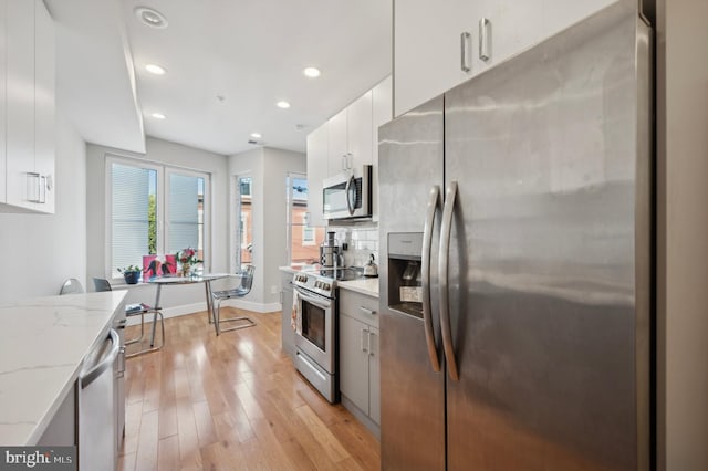 kitchen featuring white cabinets, decorative backsplash, light stone countertops, light wood-type flooring, and appliances with stainless steel finishes