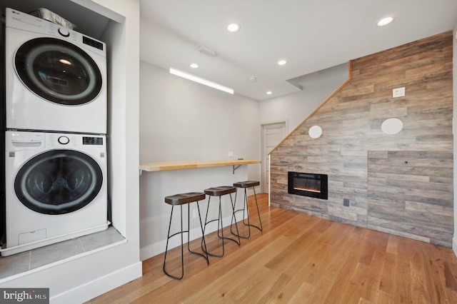 laundry room featuring stacked washing maching and dryer, light wood-type flooring, and a tile fireplace