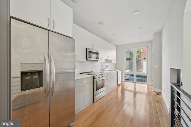 kitchen with stainless steel appliances, white cabinetry, sink, light hardwood / wood-style flooring, and decorative backsplash