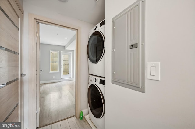 washroom with electric panel, stacked washer and dryer, and light hardwood / wood-style flooring