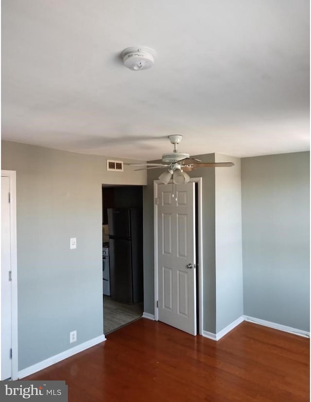 unfurnished room with ceiling fan, wood finished floors, visible vents, and baseboards