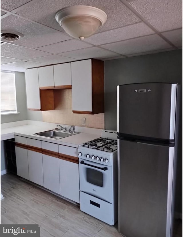 kitchen featuring white range with gas stovetop, light countertops, freestanding refrigerator, white cabinets, and a sink