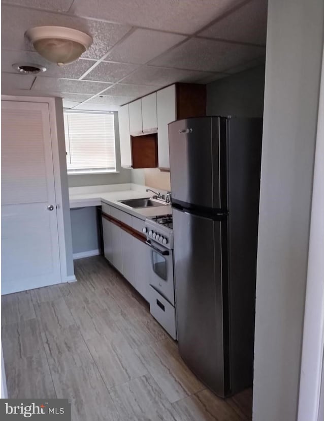 kitchen with white gas stove, light countertops, freestanding refrigerator, white cabinetry, and a sink