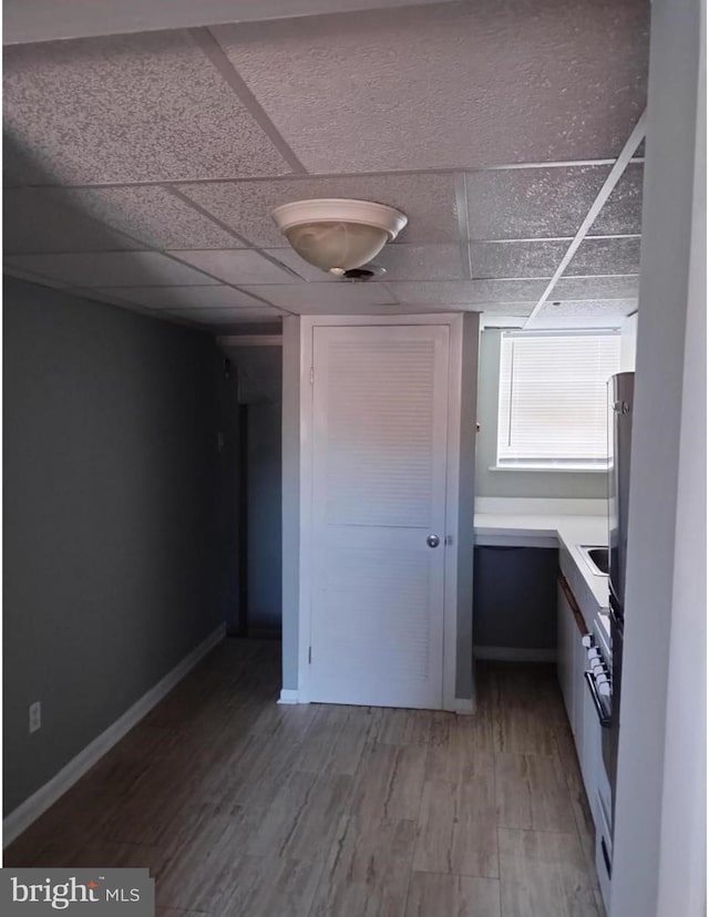 interior space with light wood finished floors, a drop ceiling, and baseboards