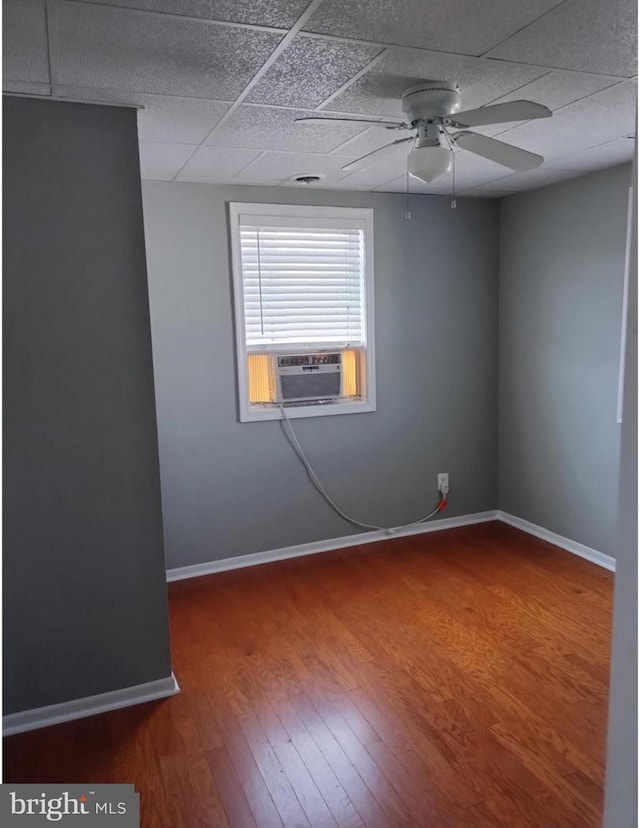 spare room featuring wood finished floors, cooling unit, a paneled ceiling, baseboards, and ceiling fan