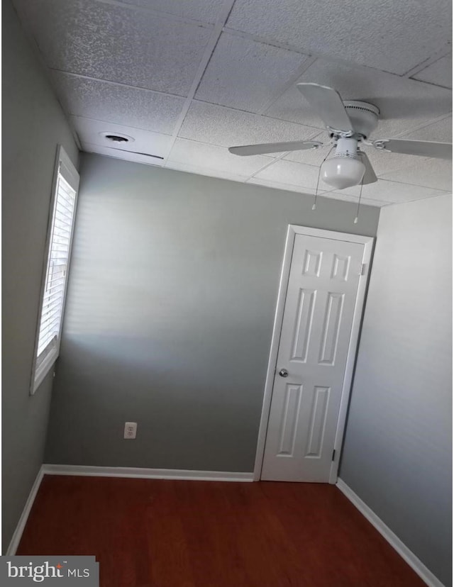 unfurnished room with a drop ceiling, baseboards, wood finished floors, and a ceiling fan