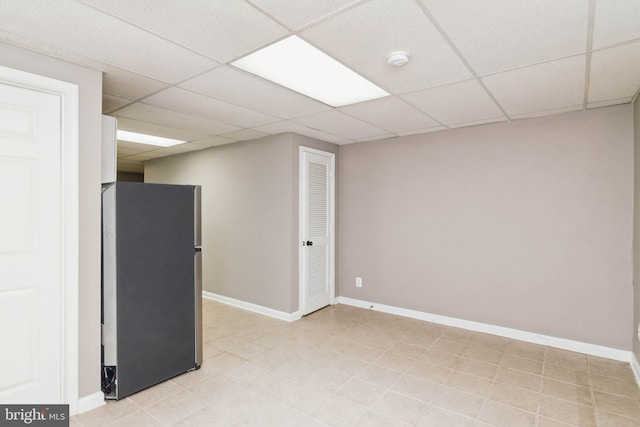 finished basement with a drop ceiling, freestanding refrigerator, and baseboards