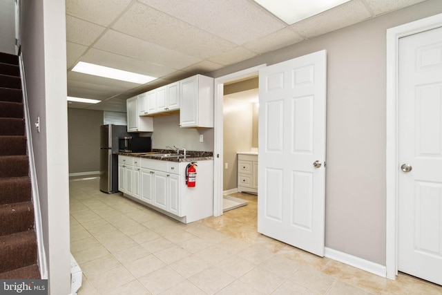 kitchen featuring a sink, a drop ceiling, freestanding refrigerator, and white cabinetry