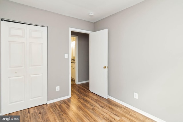 unfurnished bedroom featuring wood finished floors, baseboards, and a closet