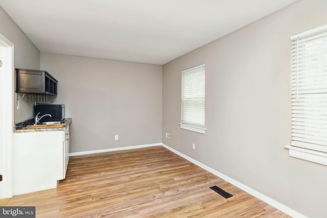 unfurnished dining area featuring light wood finished floors, visible vents, baseboards, and a sink