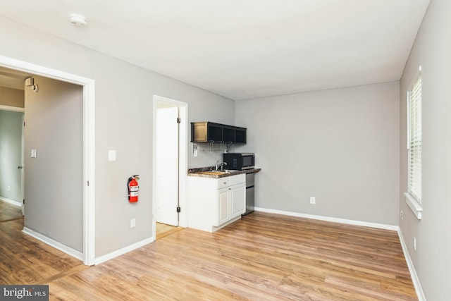 kitchen with a sink, baseboards, light wood-style flooring, and black microwave