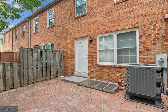 doorway to property with brick siding, central AC unit, and fence