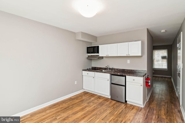 kitchen with light wood finished floors, white cabinets, freestanding refrigerator, and a sink