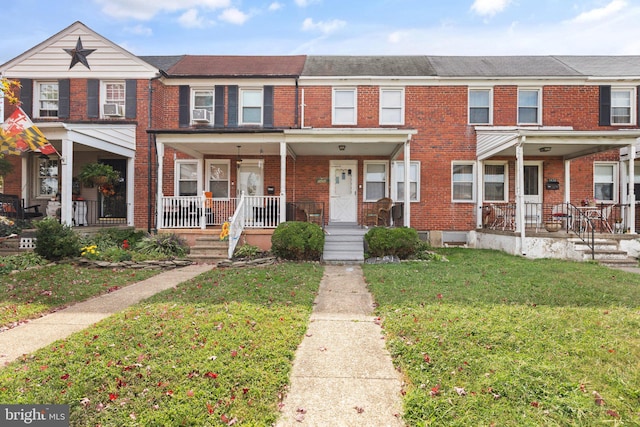 townhome / multi-family property featuring cooling unit, brick siding, covered porch, and a front lawn