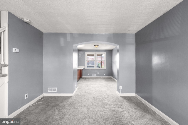 carpeted empty room featuring arched walkways, visible vents, a textured ceiling, and baseboards