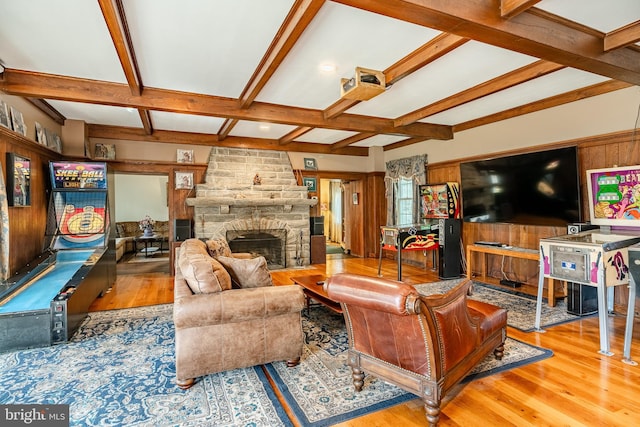 living room with coffered ceiling, wood walls, a stone fireplace, wood-type flooring, and beam ceiling