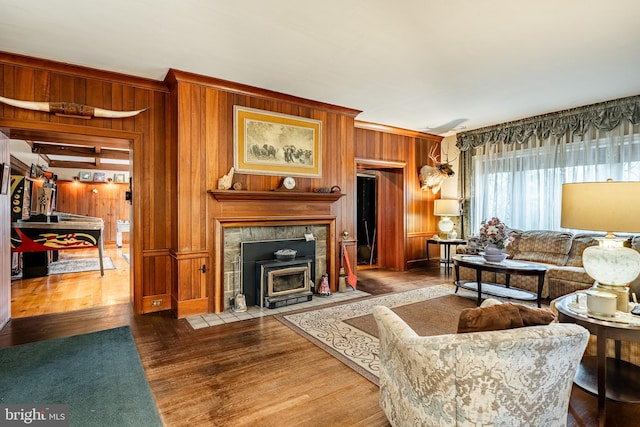 living room featuring a tiled fireplace, crown molding, hardwood / wood-style floors, and wooden walls